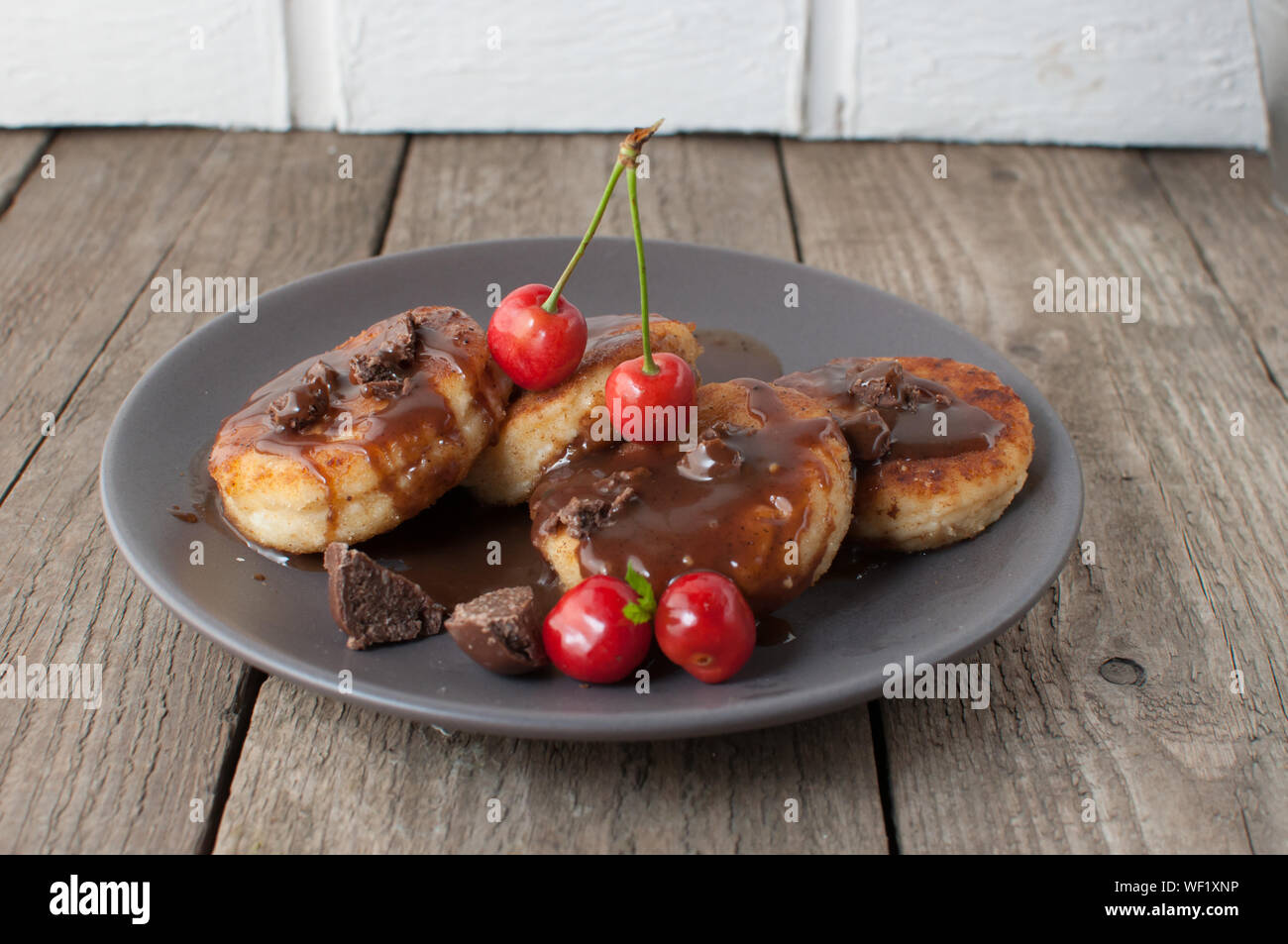 Colazione Gourmet - frittelle di cagliata, cheesecake, cagliata frittelle con ciliegie e cioccolato in una piastra di marrone. Salubre dessert su una tavola di legno in un r Foto Stock