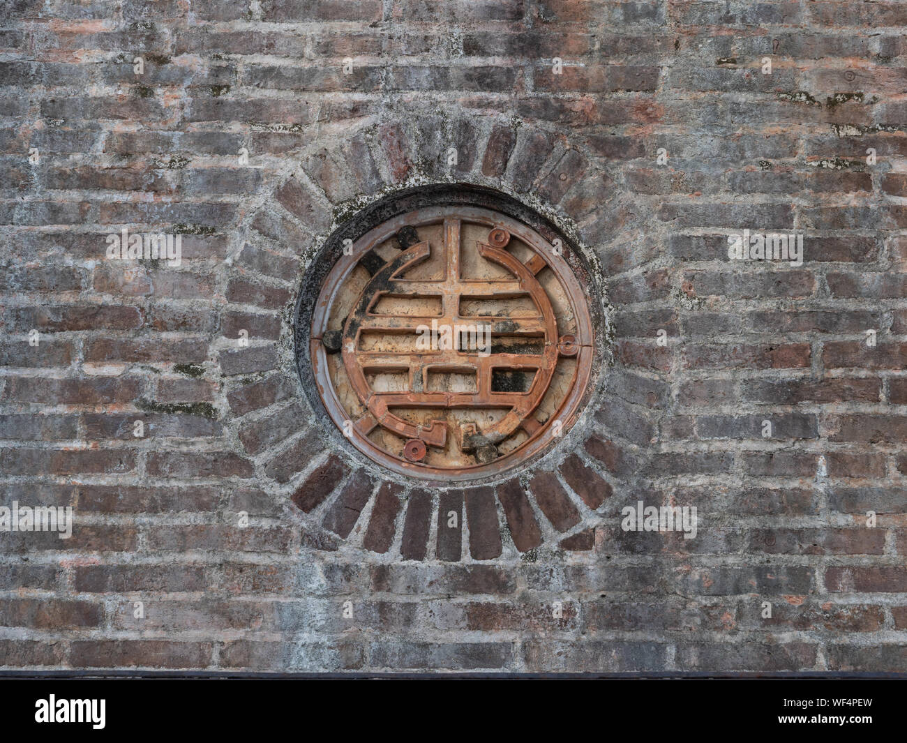 Close up di un medaglione in metallo con disegno geometrico o set di caratteri in un muro di mattoni nella Pagoda della Signora Celeste di Hue Vietnam Foto Stock