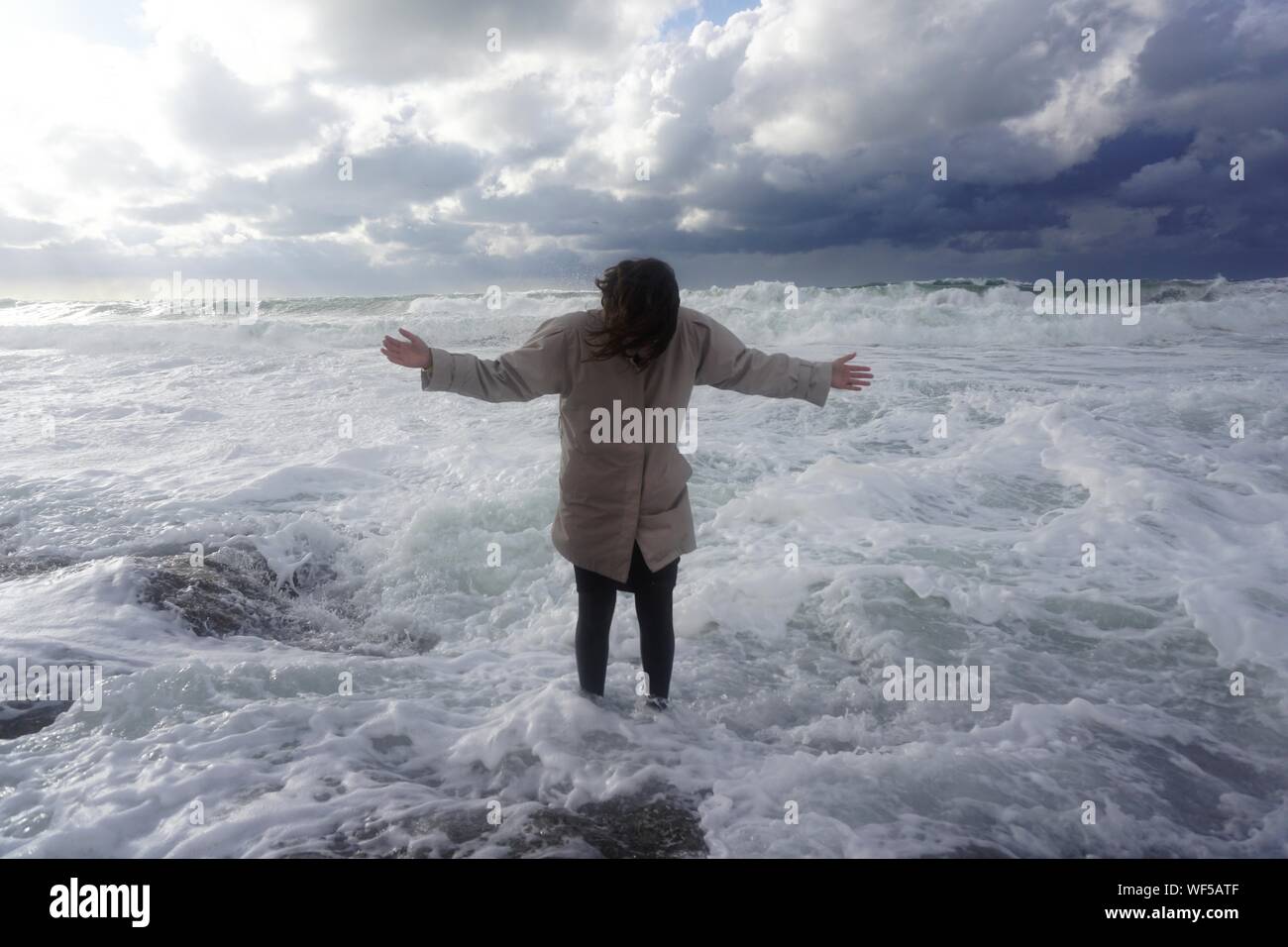 Donna con la faccia oscurata in piedi in acqua poco profonda contro le nuvole di tempesta Foto Stock