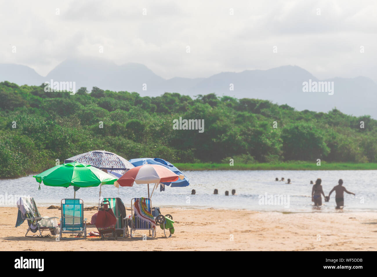 Cinque ombrelloni sono bloccato nella sabbia, alcune persone stanno avendo una nuotata nel lago solo con la loro testa di di acqua e di un margine di profitto in una foresta a Paulo Cez Foto Stock