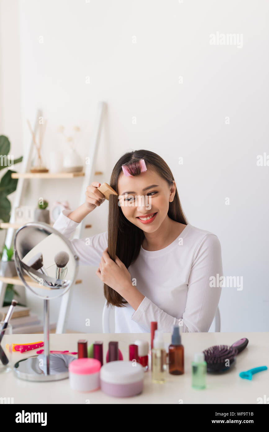 Tutorial di acconciatura. Donna asiatica spazzolare i capelli e sorridente piacevolmente durante le riprese di un tutorial per la sua bellezza blog Foto Stock