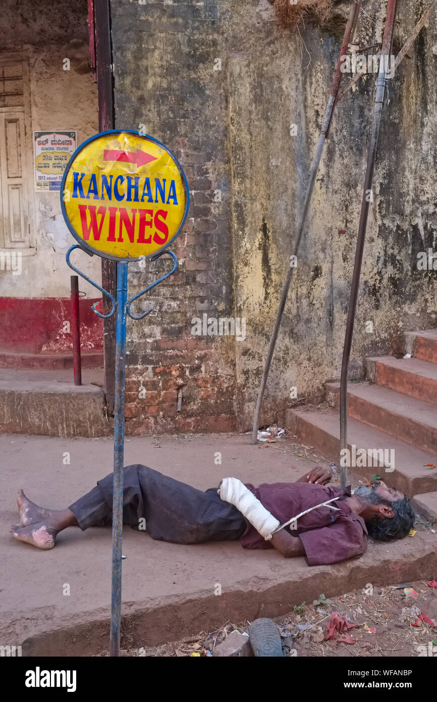 Un bendato, apparentemente obliviously uomini ubriachi su un marciapiede accanto al cartello che indica a un negozio di liquori a pochi passi; di Mangalore, Karnataka, India Foto Stock