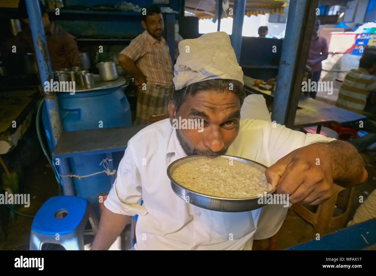 Un uomo in un piccolo ristorantino di Mangalore (Mangaluru), Karnataka, India, slurping fino una piastra di ganji o farinata di riso a livello locale un piatto di pinzatura Foto Stock
