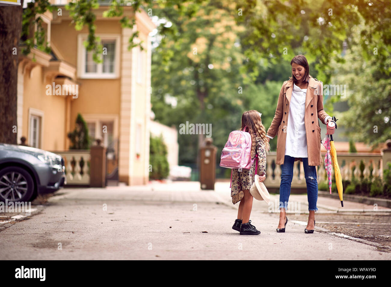 Carino bambina con zaini andando a scuola con sua madre sorridente Foto Stock