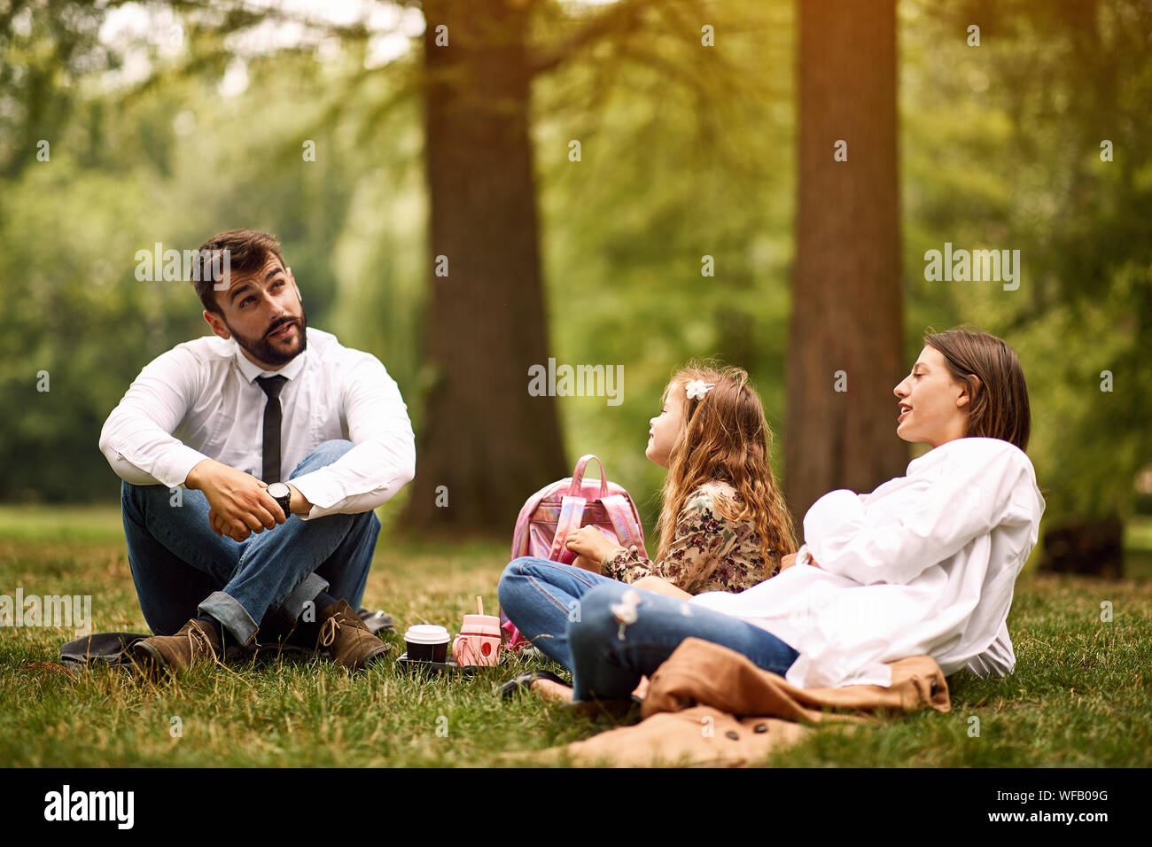 Felice il padre e la madre con la loro figlia dopo il lavoro e la scuola seduto e appoggiato al parco. Foto Stock