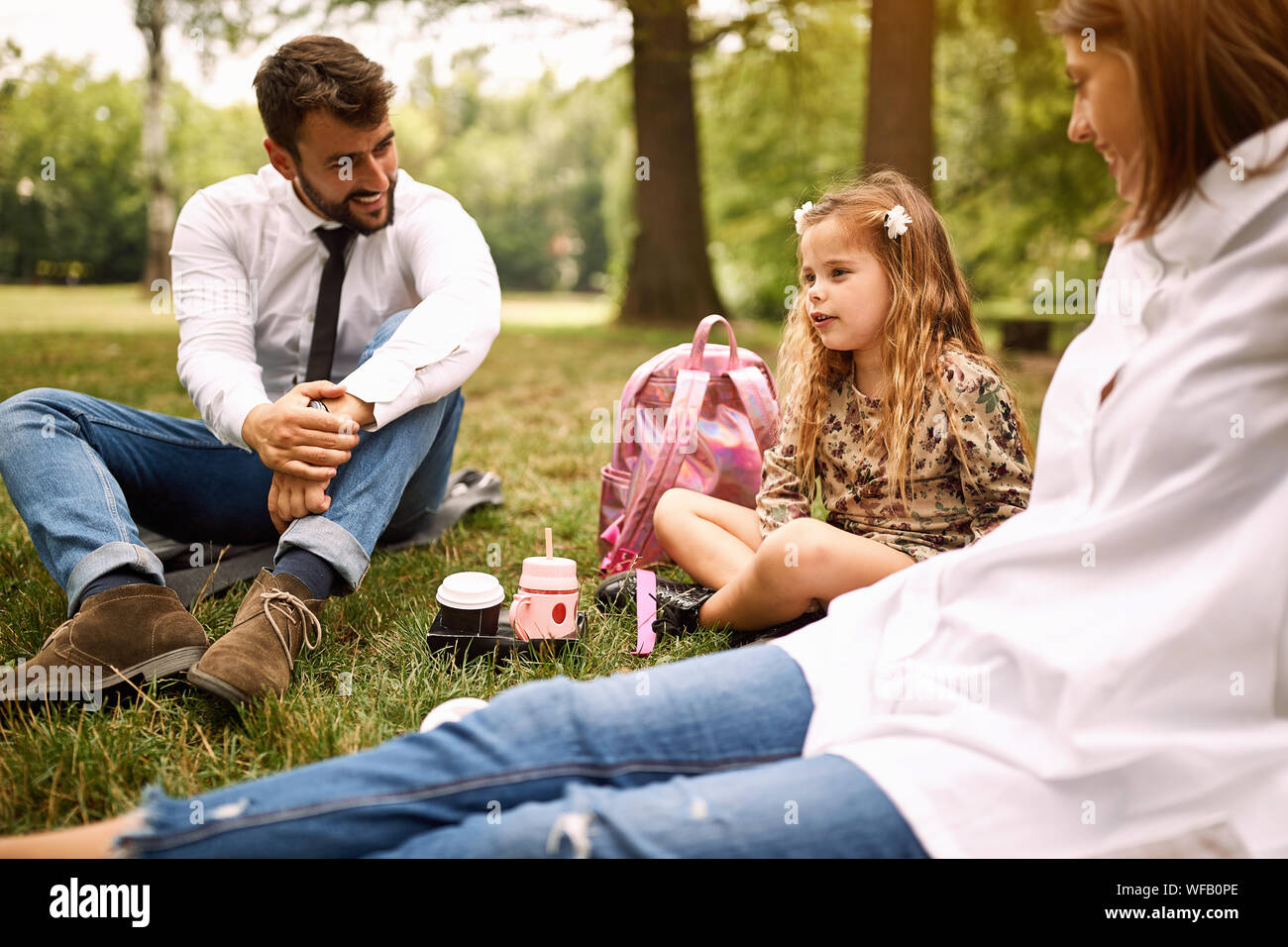 Carino figlia con i loro genitori e seduta in appoggio al parco. Foto Stock