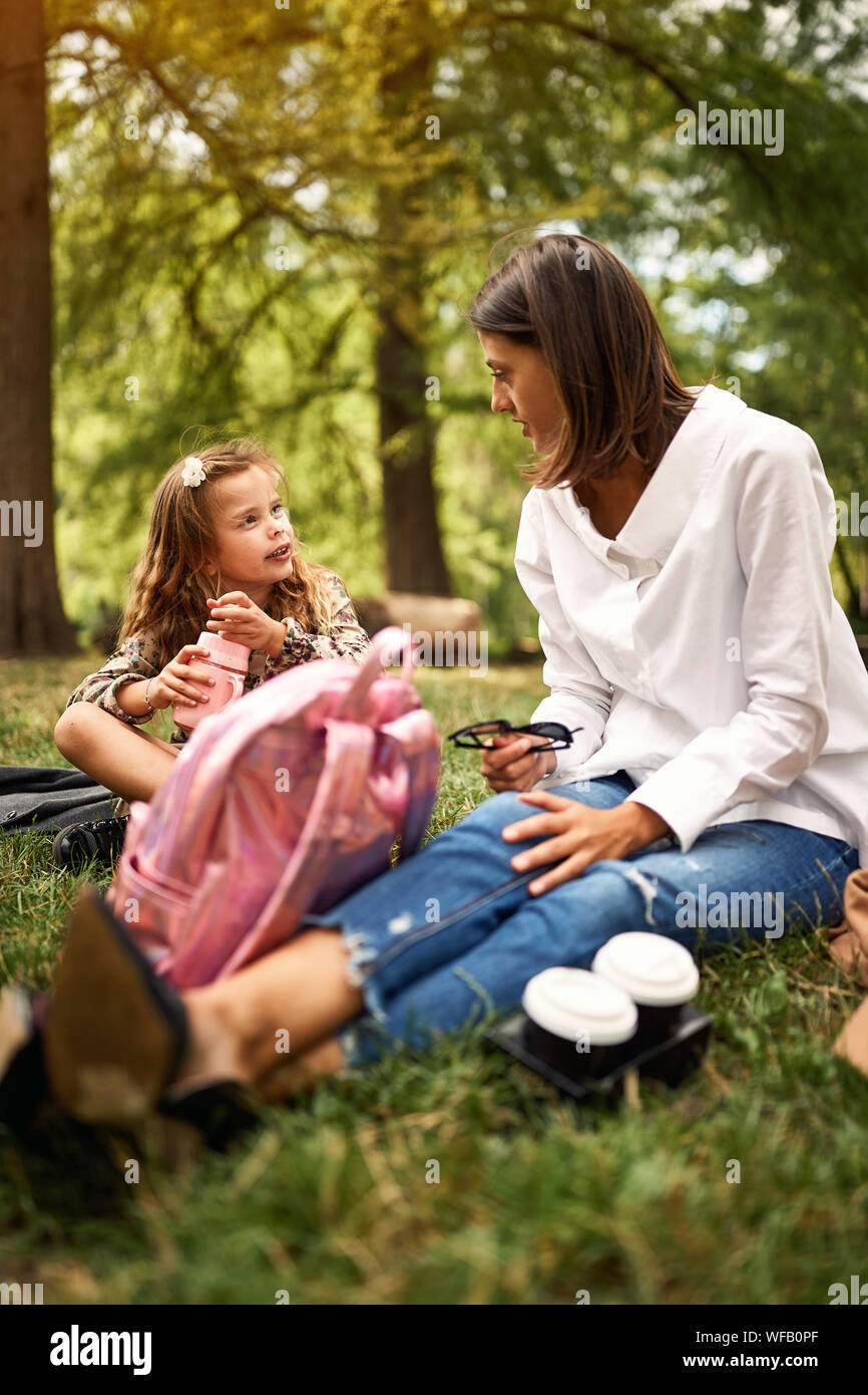 Carino figlia con la loro madre seduto e appoggiato al parco. Foto Stock