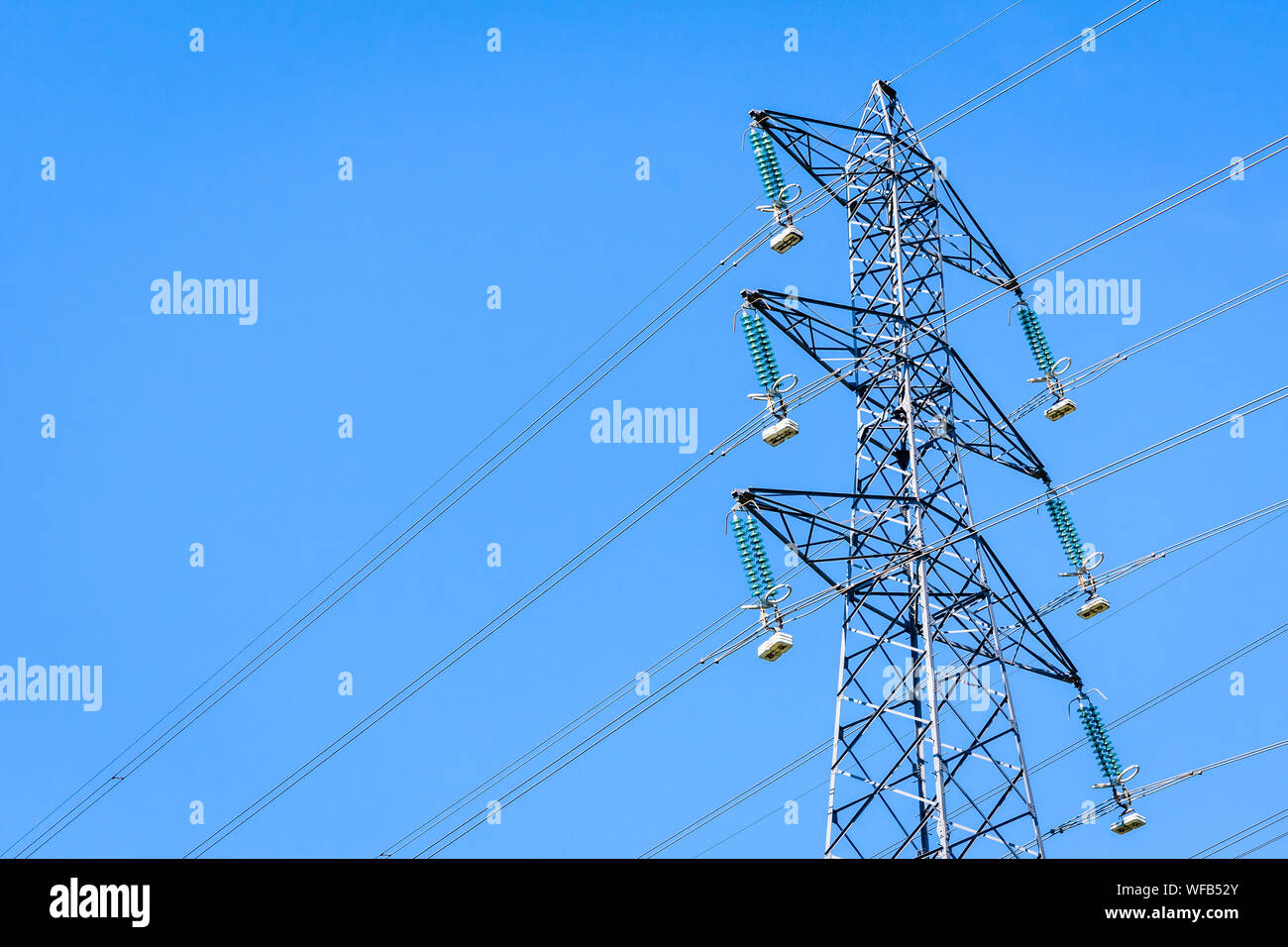 Vista dal basso di un elettricità traliccio supportante un overhead di alta tensione della linea di alimentazione contro il cielo blu. Foto Stock