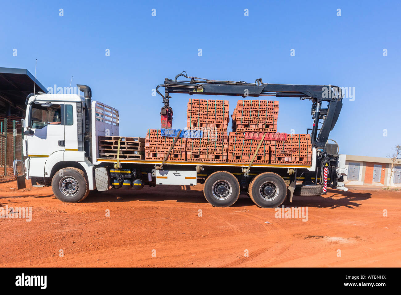 Il nuovo colore rosso dei mattoni di argilla blocchi sollevata dalla gru su autocarro rimorchio per veicoli per la consegna alla costruzione dell'edificio sito nel mattino cielo blu. Foto Stock
