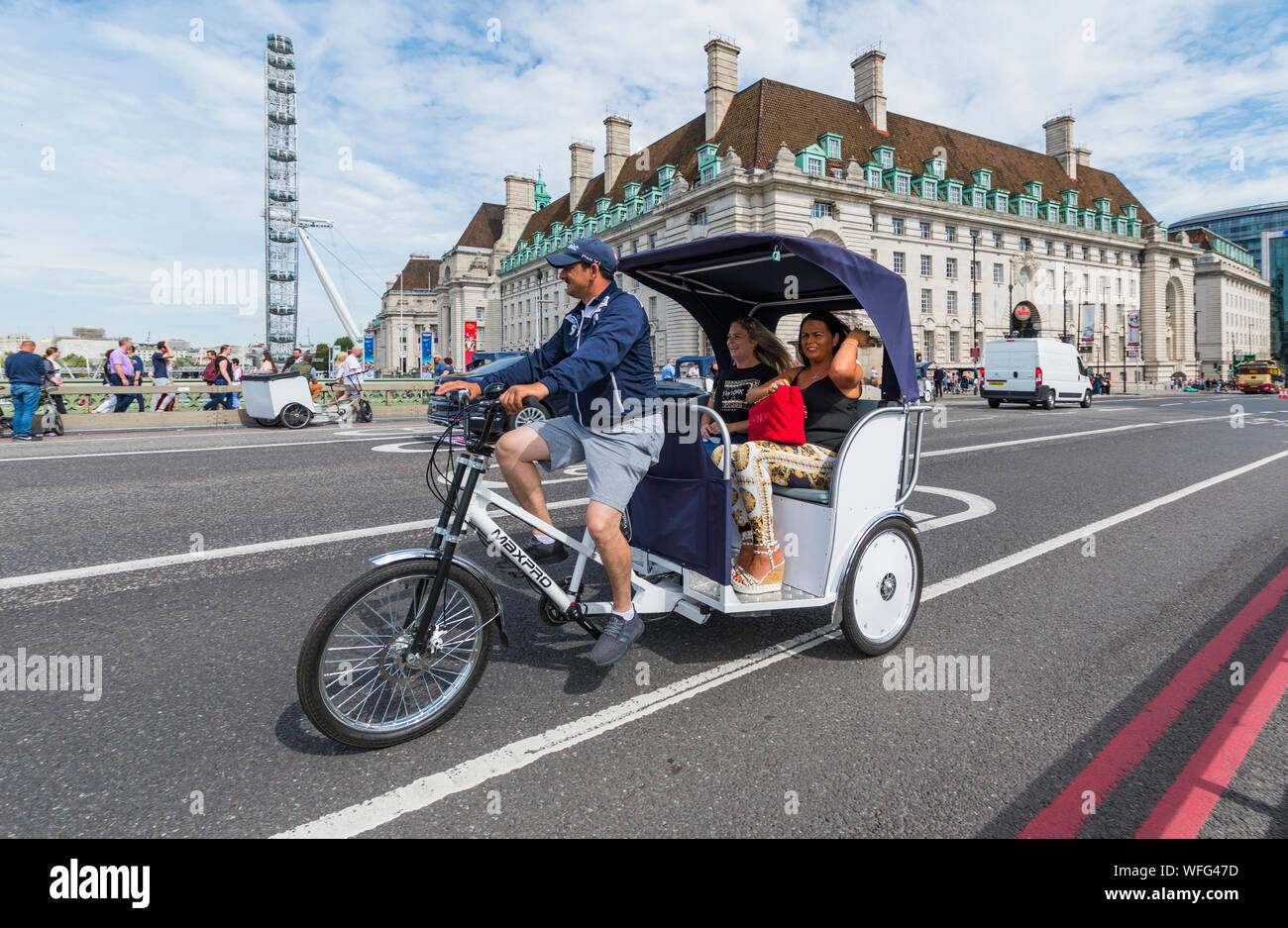 I turisti come passeggeri in un giro turistico in un 3 ruote o Rickshaw Pedicab attraverso Westminster Bridge nella City di Londra, Inghilterra, Regno Unito. Foto Stock