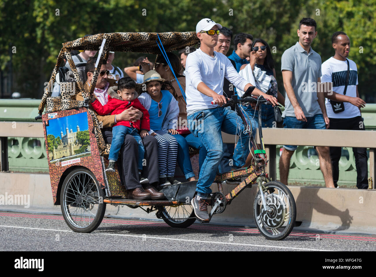 I turisti come passeggeri in un giro turistico in un 3 ruote o Rickshaw Pedicab attraverso il ponte di Westminster a Londra, Inghilterra, Regno Unito. Foto Stock
