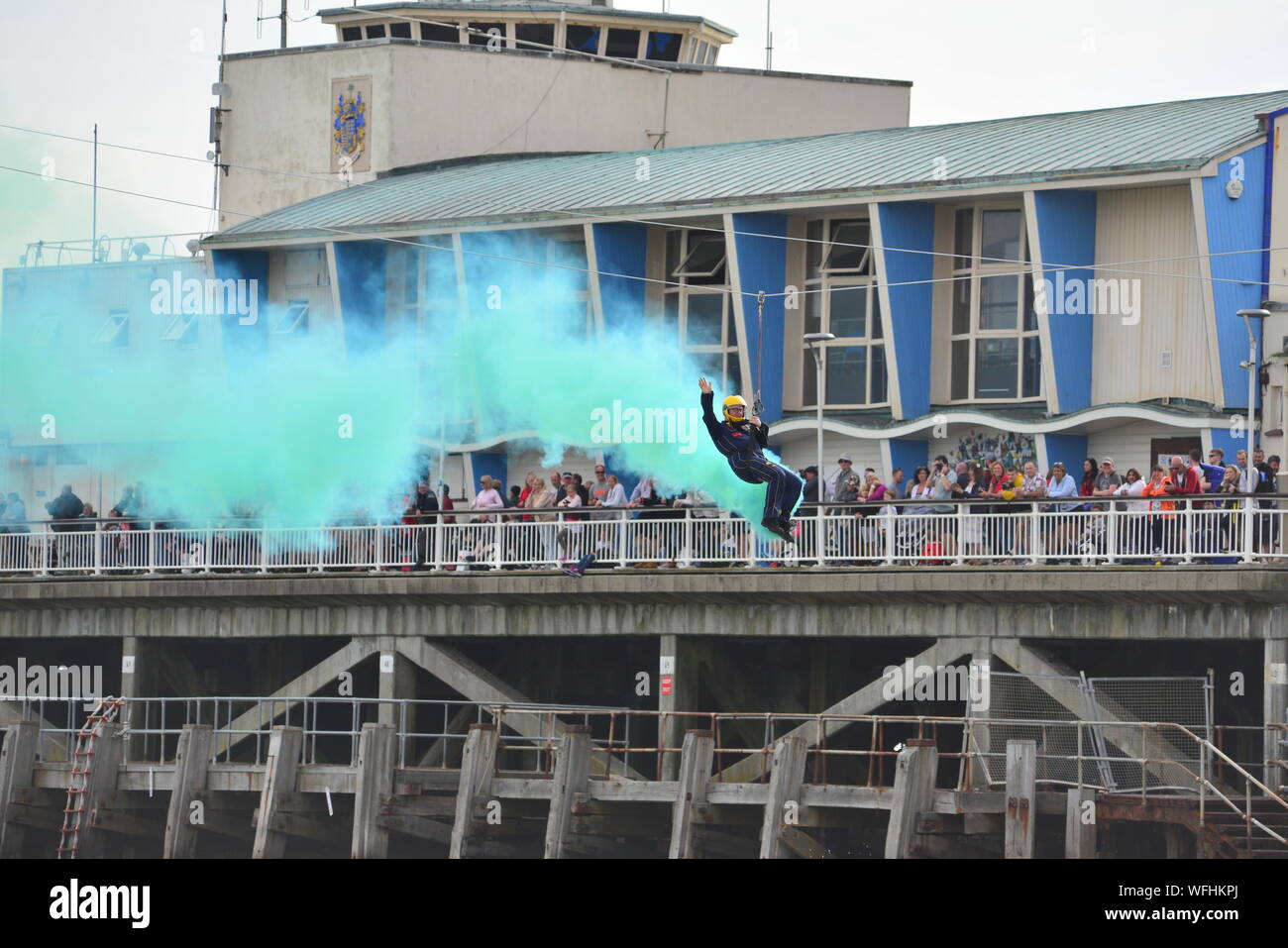 Un pilota di zip wire che esce dal fumo verde fluorescente di fronte alla folla sul molo al Bournemouth Air Festival, 2019 Foto Stock