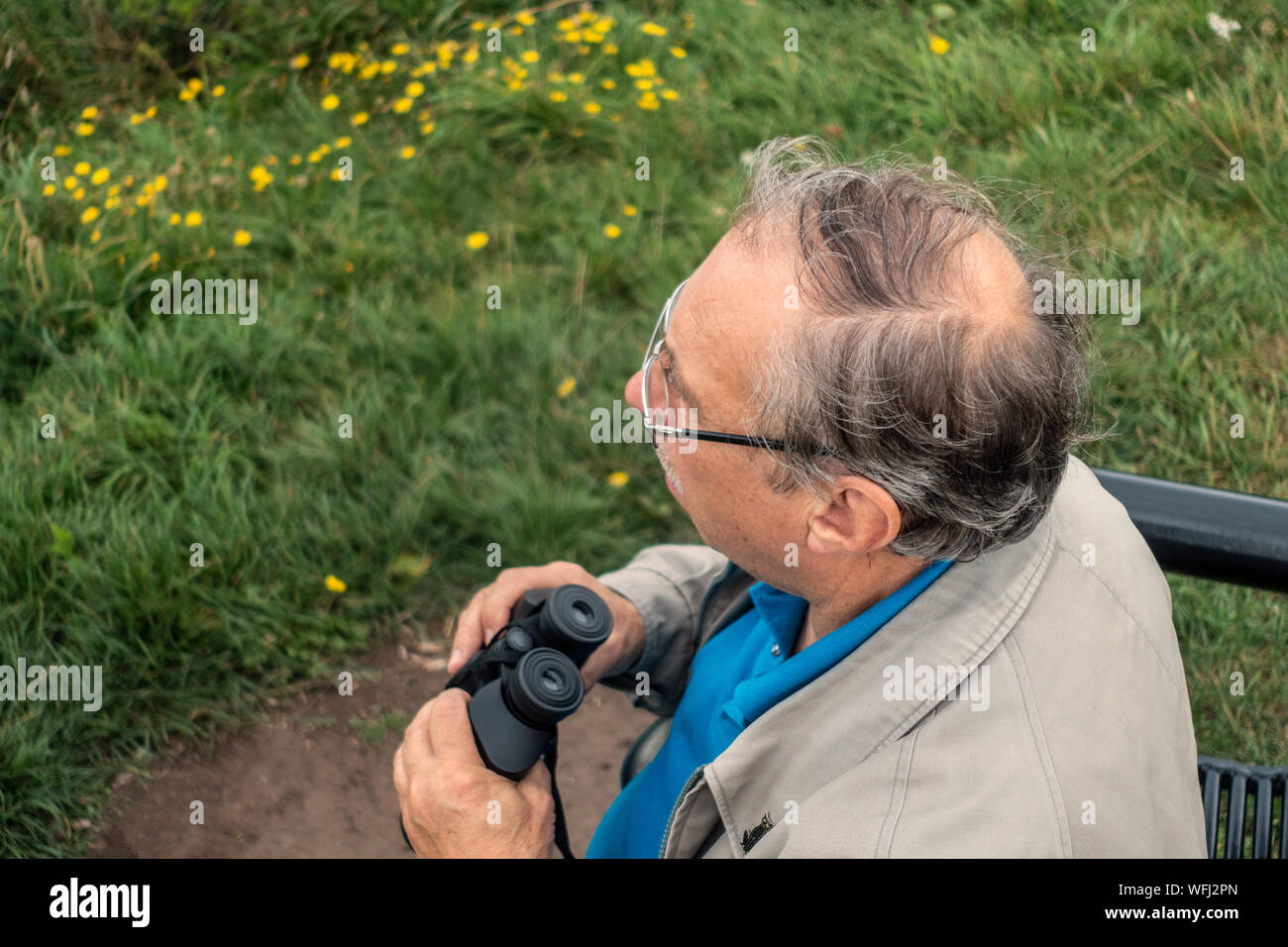 Train spotting uomo anziano con un binocolo guardando i treni Foto Stock