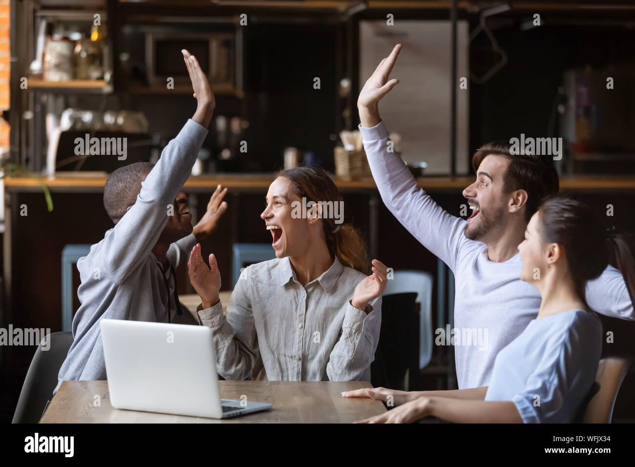 Diversi amici festeggiare la vittoria guarda il gioco sul computer portatile in cafe Foto Stock