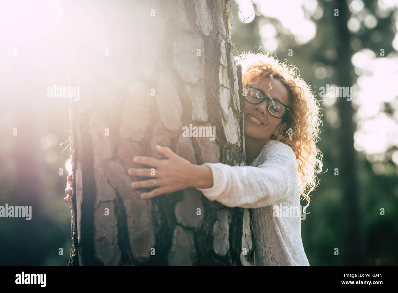 Bella donna con gli occhiali che abbraccia un grande albero con amore e con affetto - Salvare il concetto di foresta e stile di vita - per adulti in montagna o in un parco Foto Stock