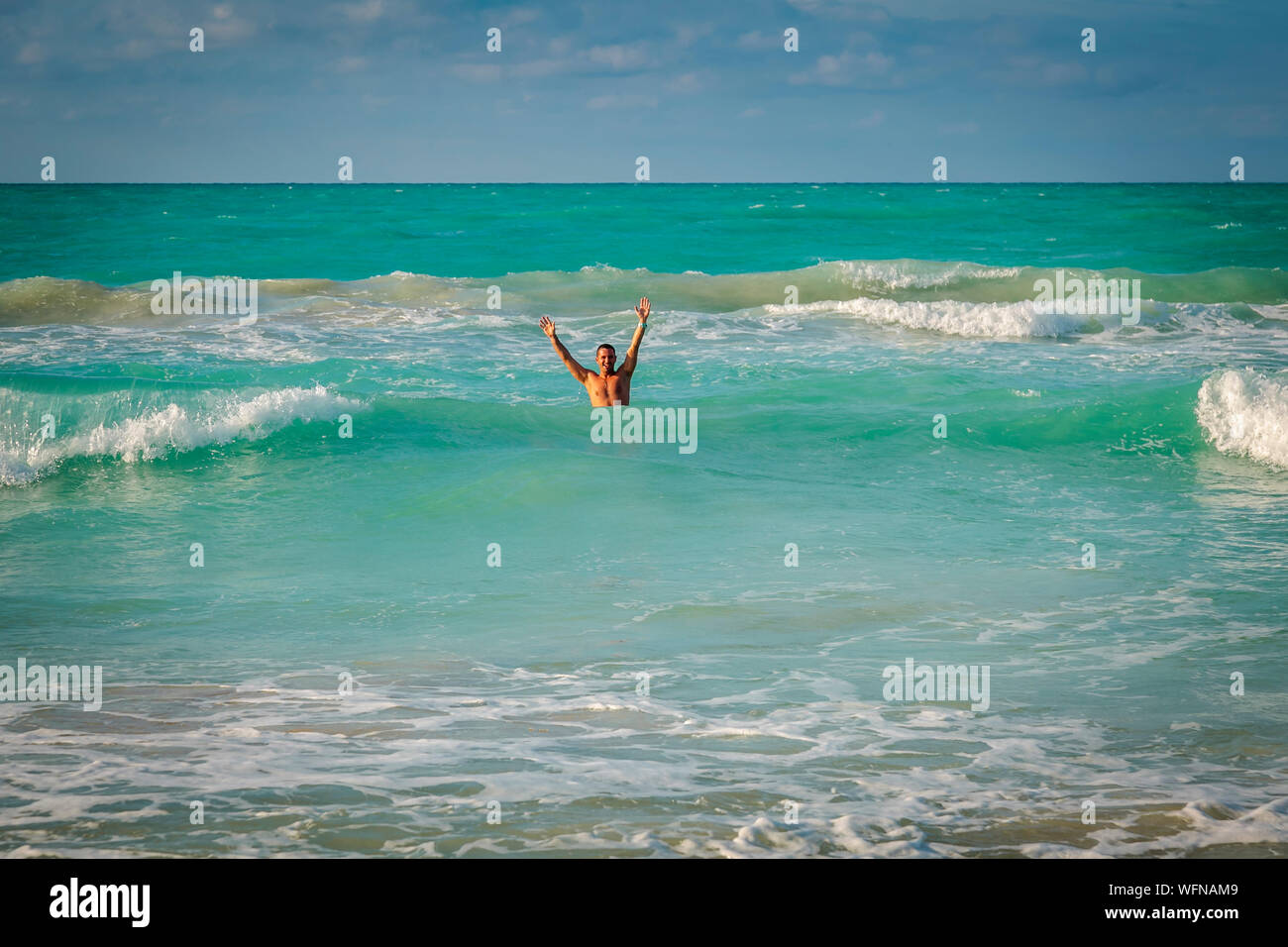 Voce maschile vacanziere nel mare che ondeggia con entrambe le braccia in alto - Varadero, Cuba Foto Stock