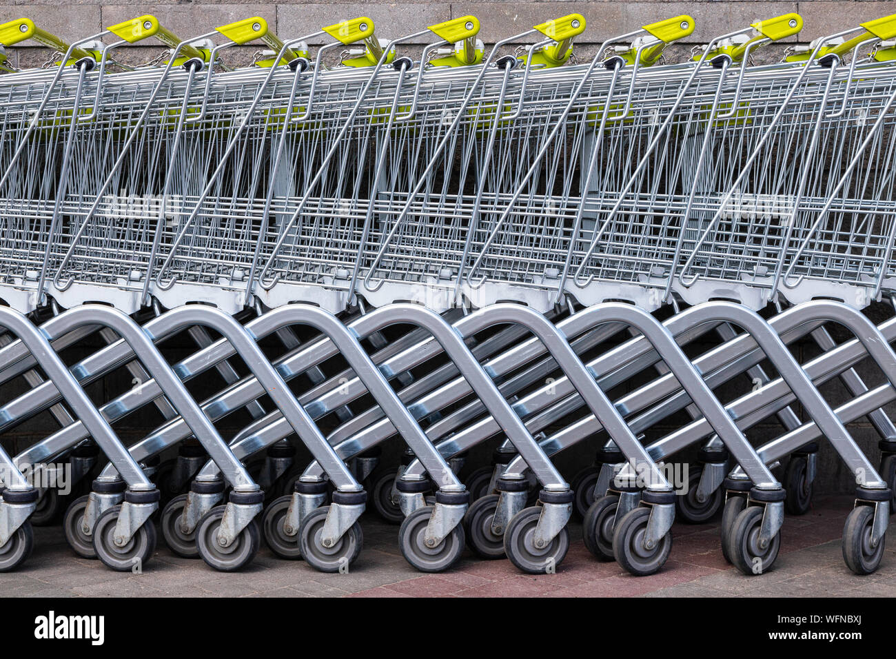 Molti grigio acciaio carrelli della spesa con le maniglie gialle in piedi in fila come sfondo per lo shopping gli argomenti delle notizie. Si erge, ruote parte inferiore, parte inferiore Foto Stock