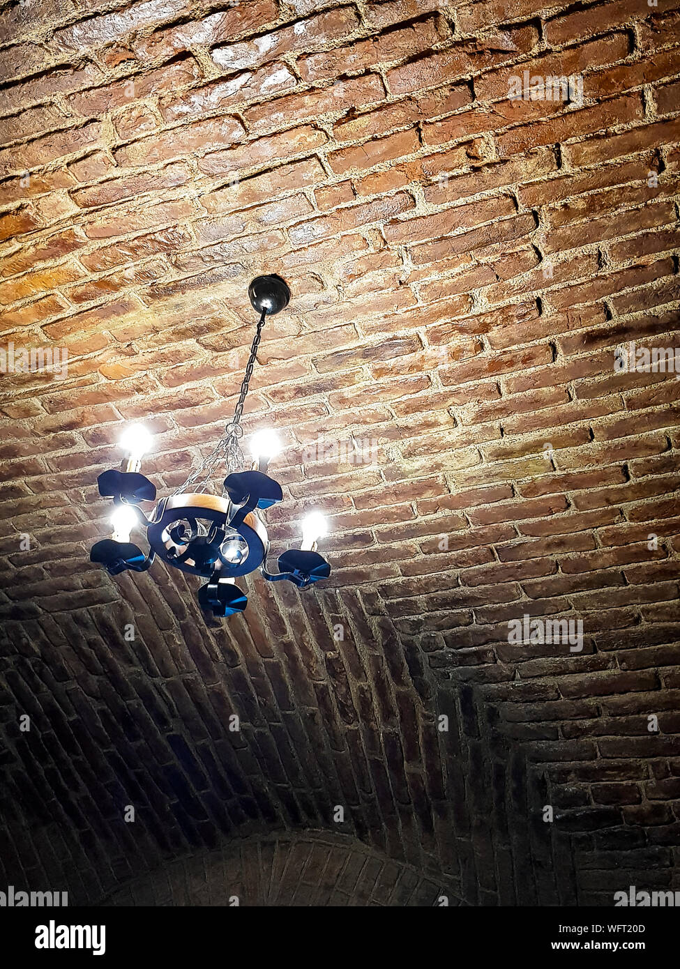 Antico lampadario di stile moderno con luci. Esso si blocca su un rosso mattone a soffitto. Rusty osservare le foto. Foto Stock