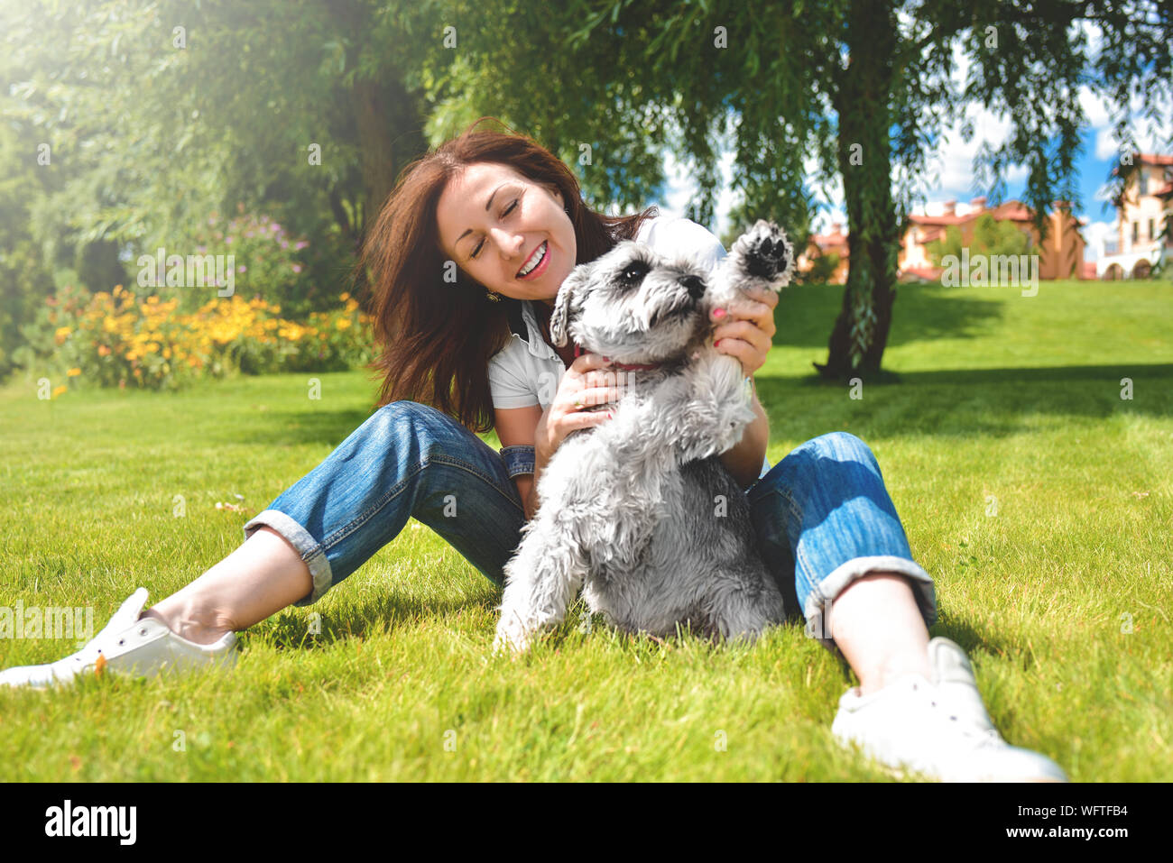 Abbastanza adulto caucasian donna felice in appoggio al parco in una giornata di sole con il suo amato cane. Laici femmina sull'erba sorridente e guardando la telecamera Foto Stock