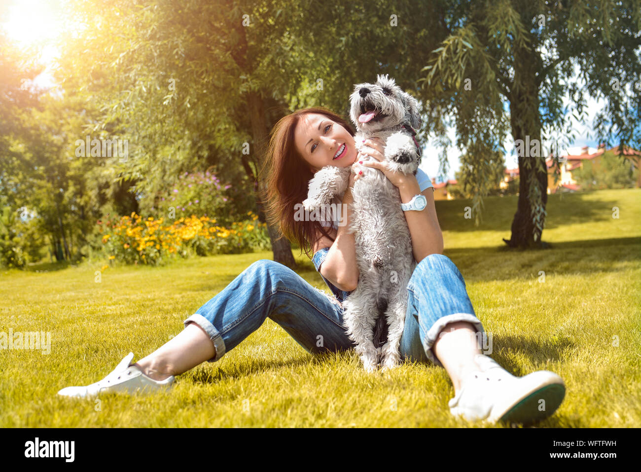 Abbastanza adulto caucasian donna felice in appoggio al parco in una giornata di sole con il suo amato cane. Laici femmina sull'erba sorridente e guardando la telecamera Foto Stock