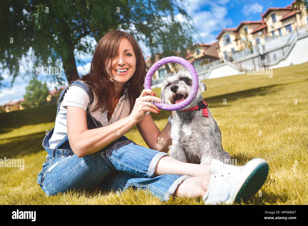Caucasian donna allegra giocando con il suo amato cane nel parco. Il concetto di amore per gli animali. migliori amici. Cane di razza Schnauzer Foto Stock