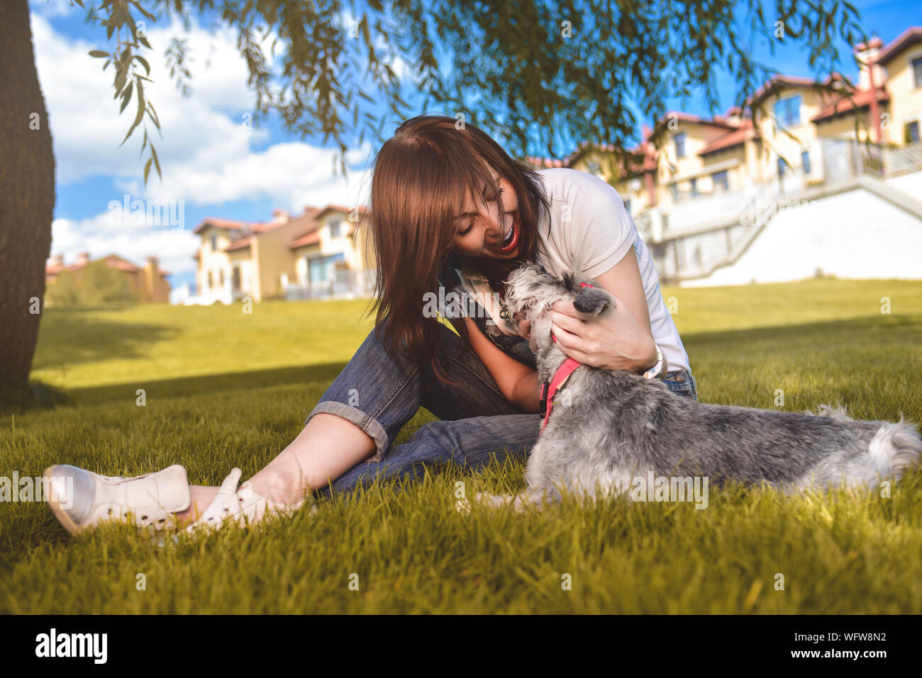 Caucasian donna allegra giocando con il suo amato cane nel parco. Il concetto di amore per gli animali. migliori amici. Cane di razza Schnauzer Foto Stock