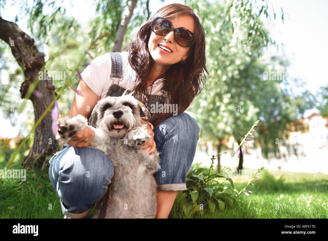 Felice donna caucasici in occhiali da sole di riposo in natura con il suo amato cane schnauzer. Foto Stock