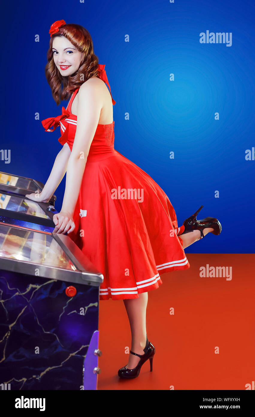 Ritratto di giovane donna in abito rosso appoggiato su di flipper Foto Stock