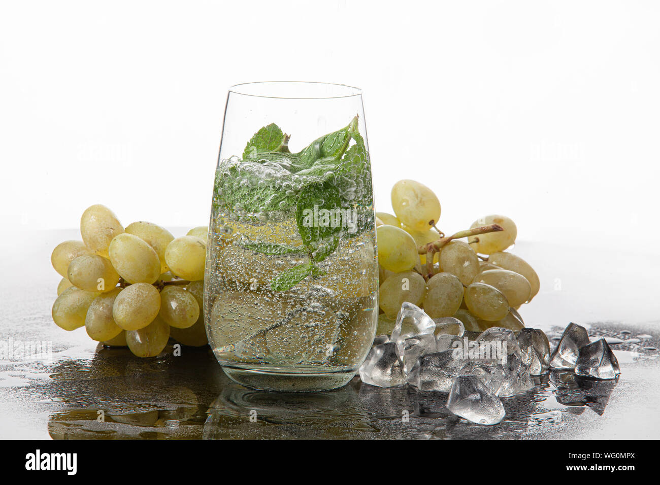 Bicchiere di acqua, di menta e di mosti di uve su un sfondo di vetro Foto Stock