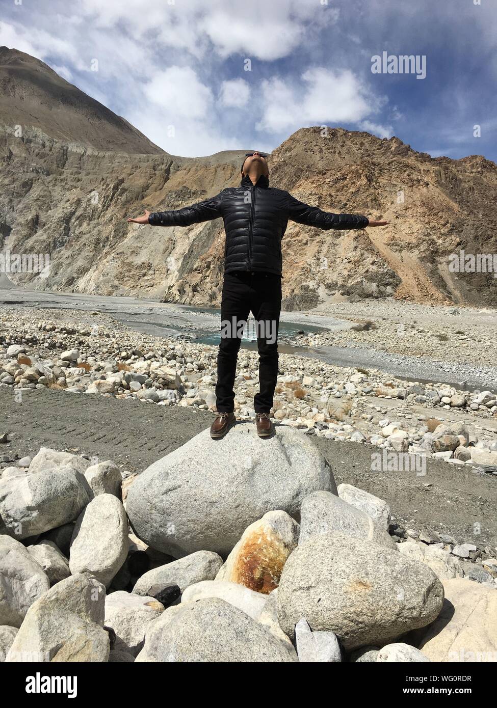 Uomo con le braccia aperte in piedi sulla pietra contro le montagne Foto Stock