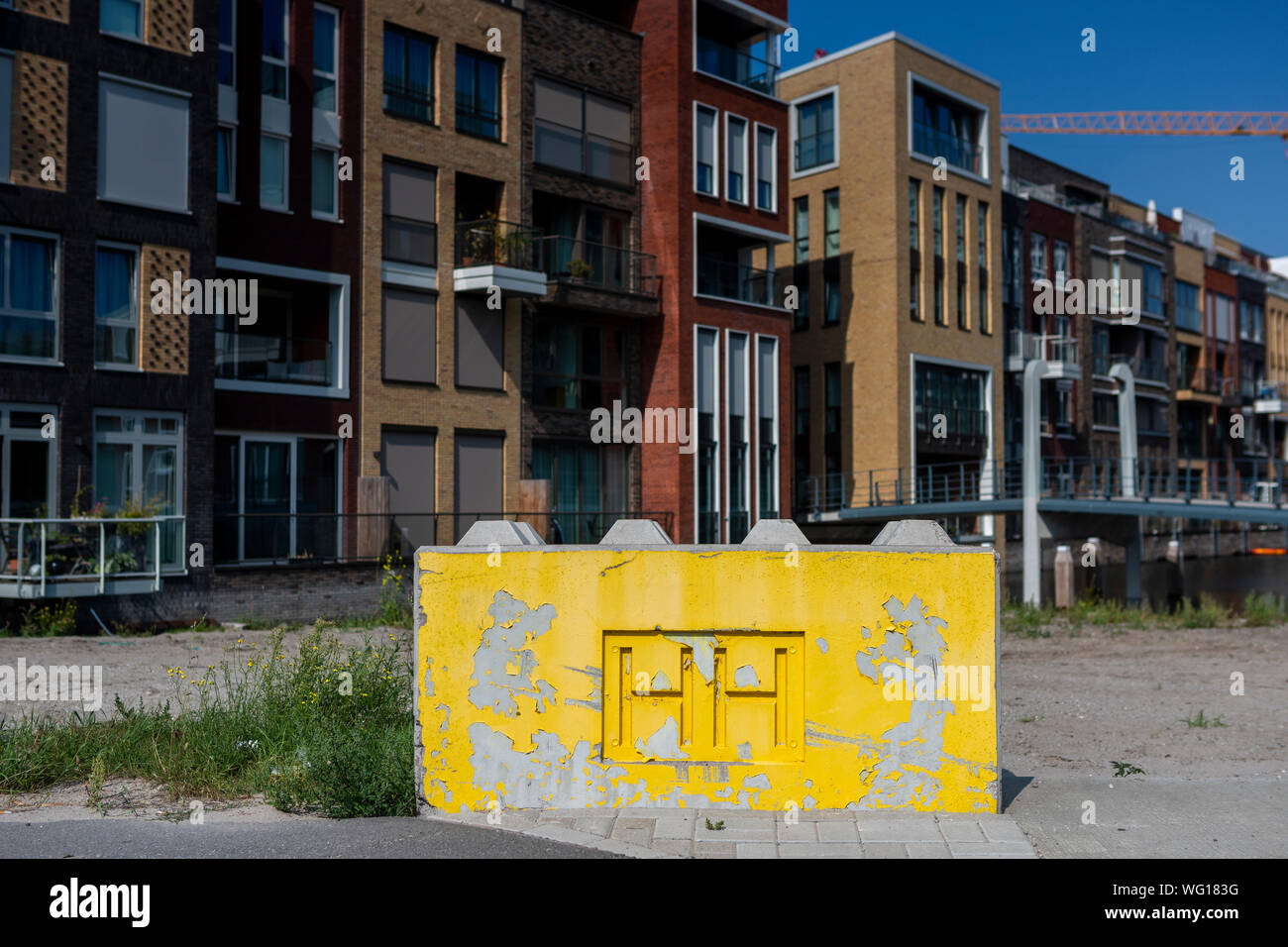 Blocco di cemento giallo come delimitazione della in costruzione Houthaven quartiere con le iniziali di HH e l'architettura contemporanea Foto Stock