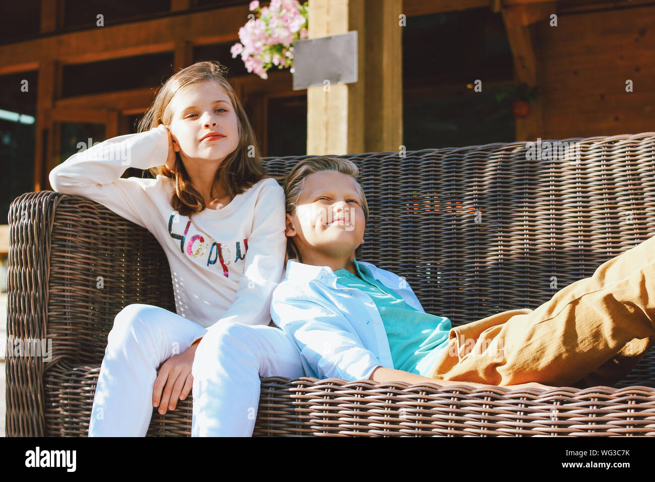 Attraente preteen bambini sorella e fratello, amici seduti sul divano in vimini nel cortile del cottage di legno Foto Stock