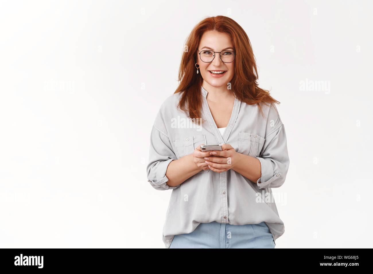 Facile app utile. Elegante Elegante redhead di mezza età imprenditrice indossare occhiali tenere lo smartphone toothy sorridente fotocamera scaricando l'applicazione SMS Foto Stock