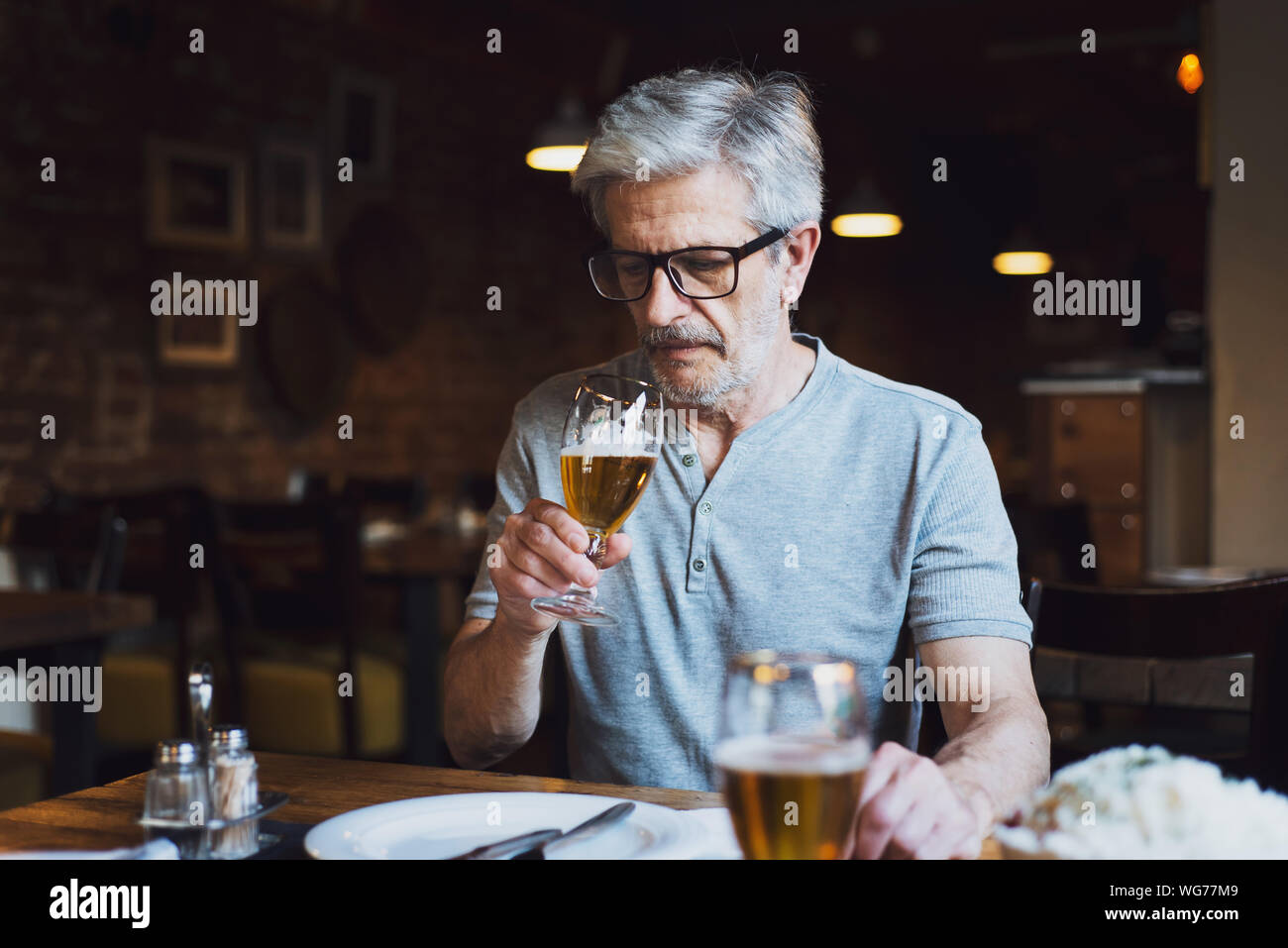 L'uomo anziano avente una birra nel bar da soli Foto Stock