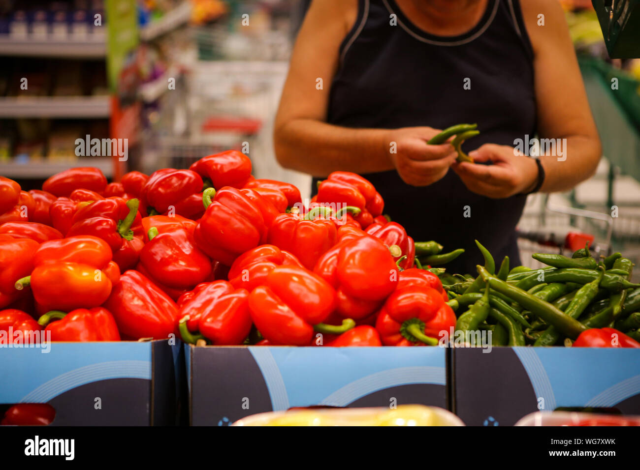 Dettagli di un uomo la scelta di peperoncini verdi piccanti (peperoni rossi dolci anche sul ripiano) sulla frutta e verdura corsia in un negozio Foto Stock