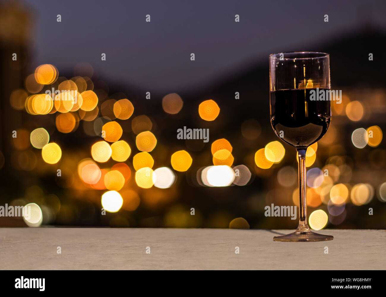 Bicchiere pieno di vino rosso su un tavolo in pietra e di fronte a qualche bella sfocato luci della città Foto Stock