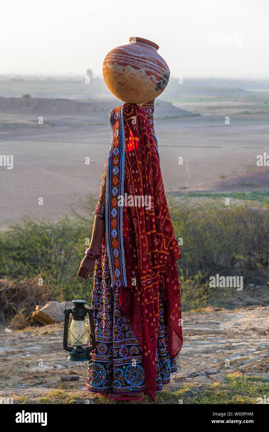 Ahir donna nei tradizionali abiti colorati che trasportano acqua in una brocca di argilla sulla sua testa, grande Rann di Kutch, Gujarat, India Foto Stock