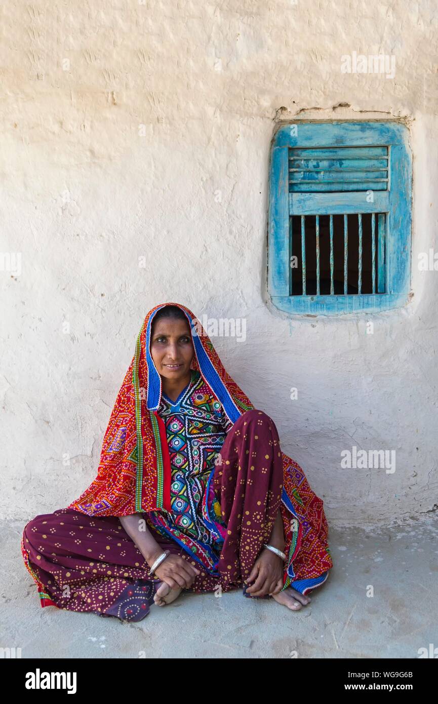 Donna nei tradizionali abiti colorati seduto contro un muro, Khavda villaggio turistico, distretto di Kutch, grande Rann di Kutch, Gujarat, India Foto Stock