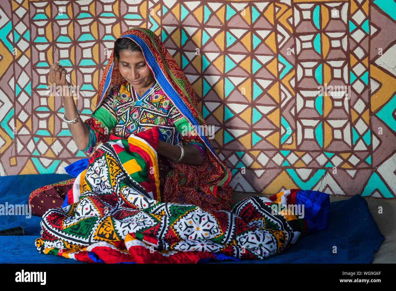 Donna in abiti tradizionali di artigianato di cucitura nella parte anteriore di una casa, Khavda villaggio turistico, distretto di Kutch, grande Rann di Kutch, Gujarat, India Foto Stock