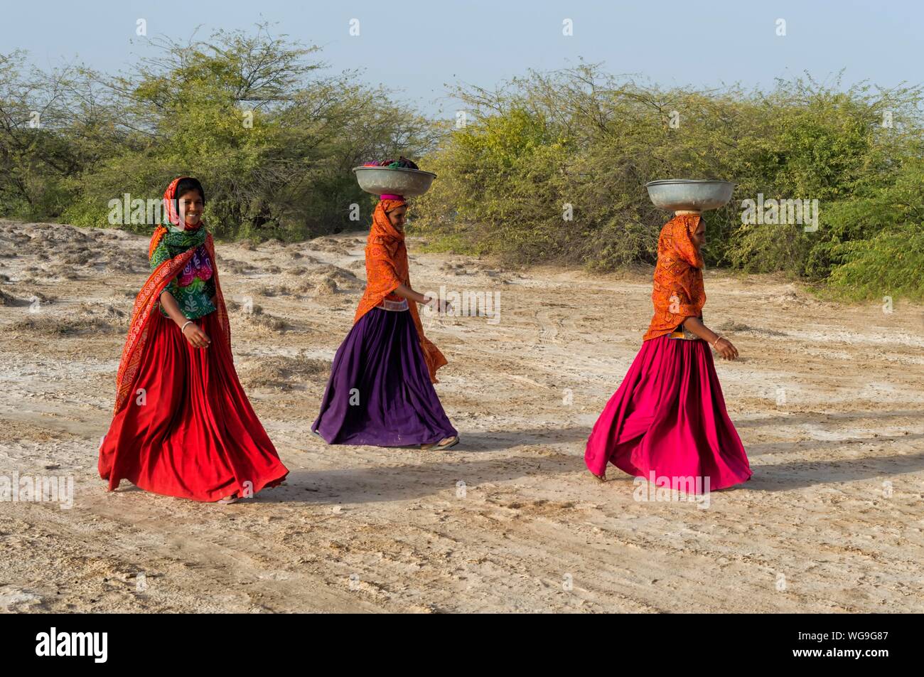 Fakirani donne nei tradizionali abiti colorati a piedi nel deserto con un bacino sul loro capo, grande Rann di Kutch, Gujarat, India Foto Stock