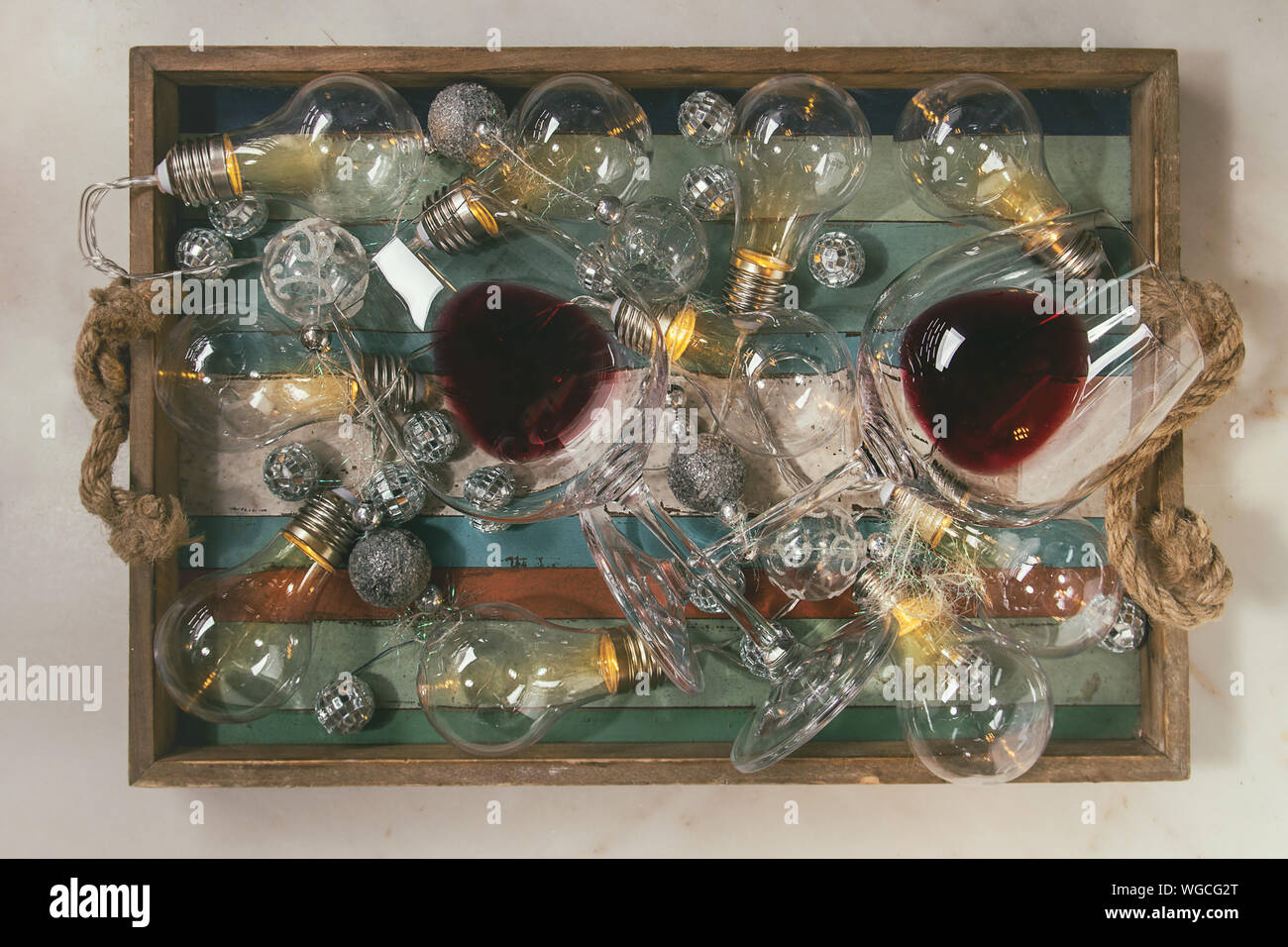 Due bicchieri di vino rosso e retrò ghirlanda di Natale con le lampade accese nel vassoio in legno su marmo bianco dello sfondo. Laici piana, spazio Foto Stock