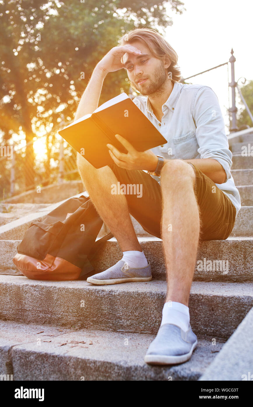 Studente di leggere un libro seduti sulle scale in campus. Girato con la sunflare Foto Stock