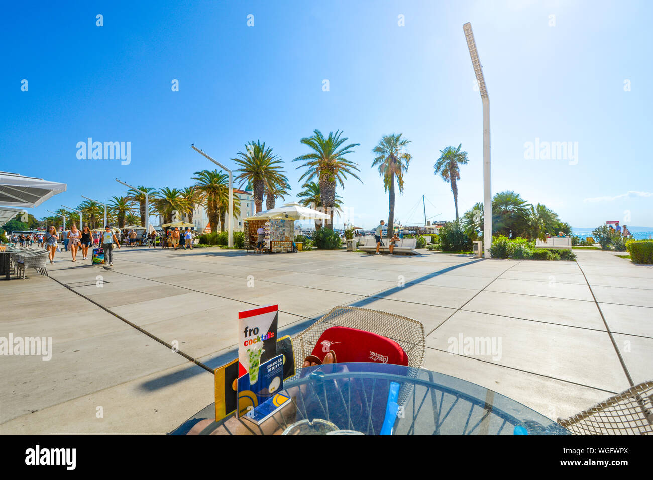 Un turista si rilassa con i loro piedi fino in corrispondenza di un marciapiede waterfront cafe sulla Riva Promenade boardwalk nell'antica città di Spalato, Croazia. Foto Stock