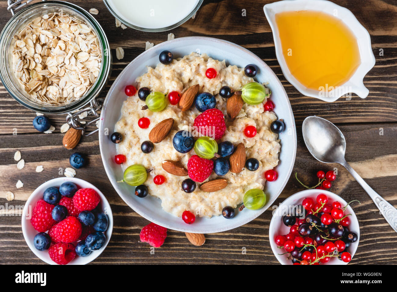 Una sana prima colazione. tazza di fiocchi d'avena porridge con frutti di bosco, noci, miele e un bicchiere di latte sulla tavola in legno rustico. vista superiore Foto Stock