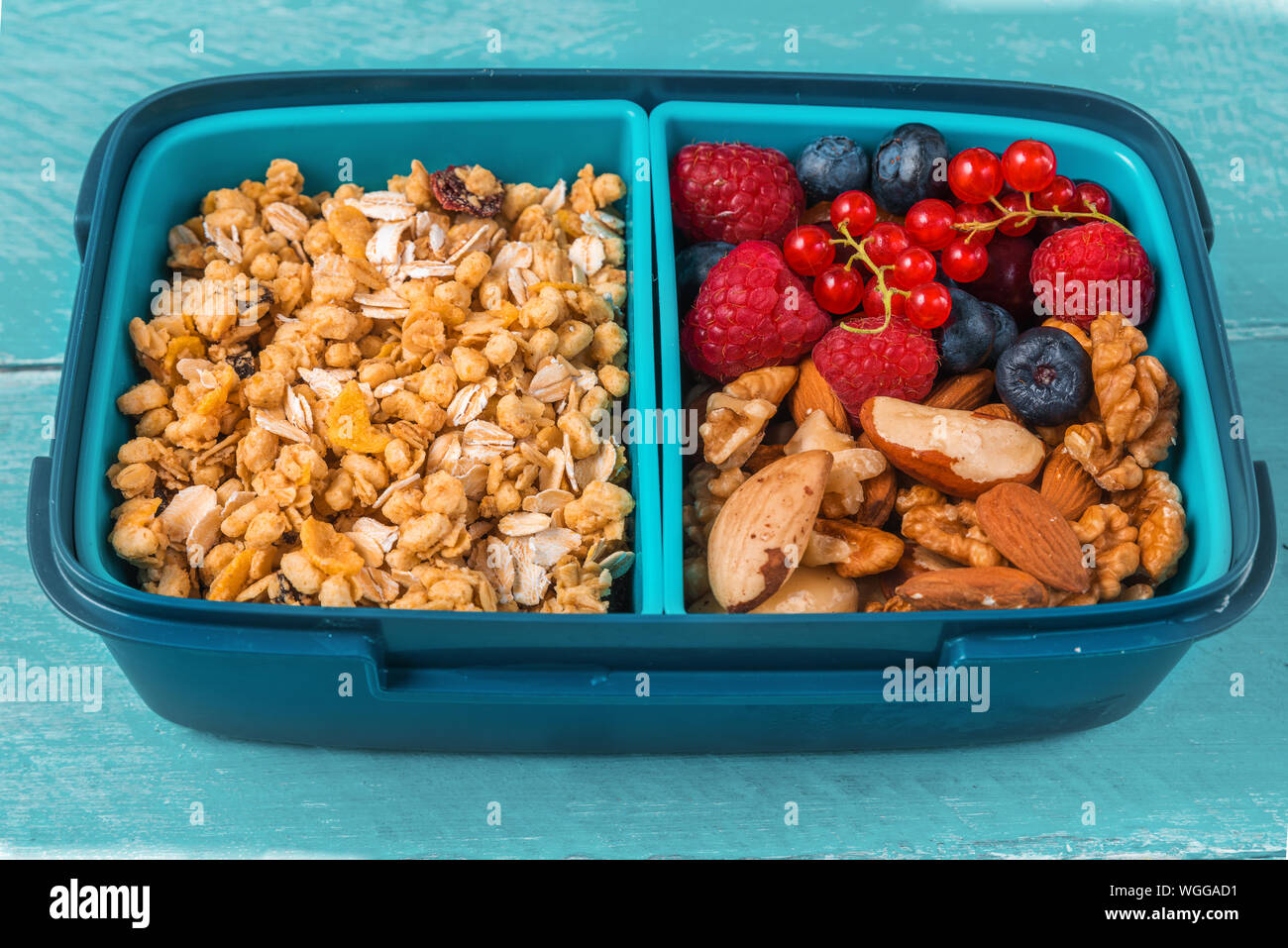 Scuola di sano scatola di pranzo con muesli, noci e bacche per fare una sana prima colazione sul blu sullo sfondo di legno. close up Foto Stock