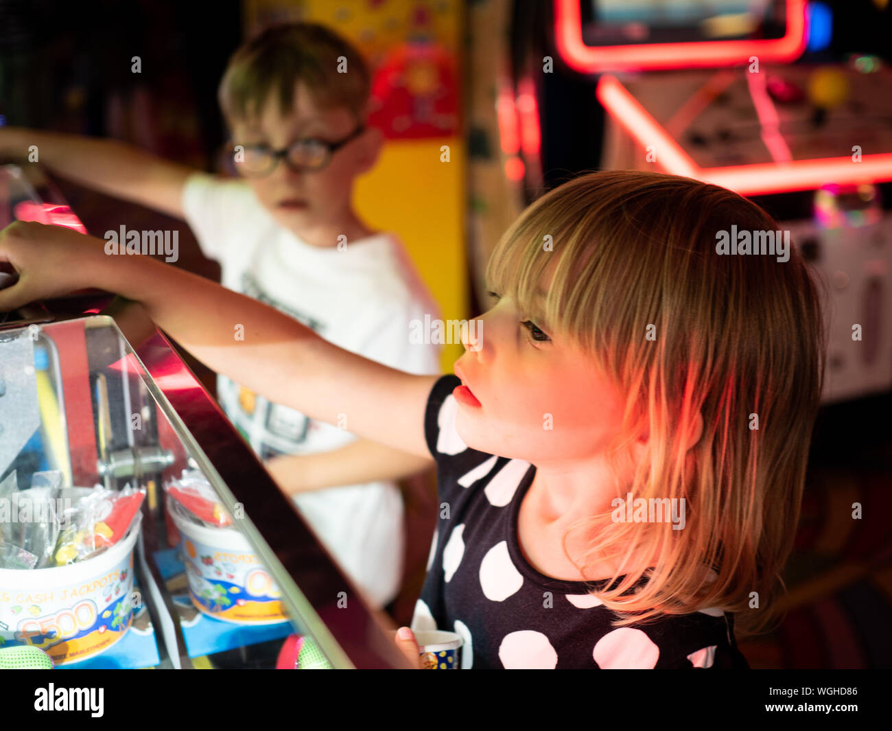 A 4 anno di età ragazza bionda gioca 2p macchine a gettoni in una città di mare di arcade con 5 anni gemelli del maschio. Foto Stock