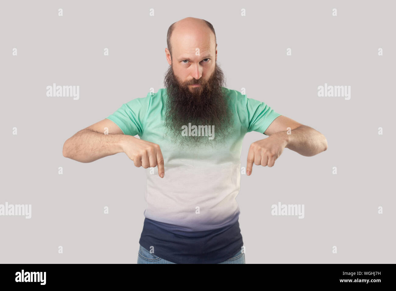 Qui e adesso! Ritratto di gravi sono di mezza età uomo calvo con barba lunga in verde chiaro t-shirt in piedi, con la punta rivolta verso il basso e cercando e comandare Foto Stock