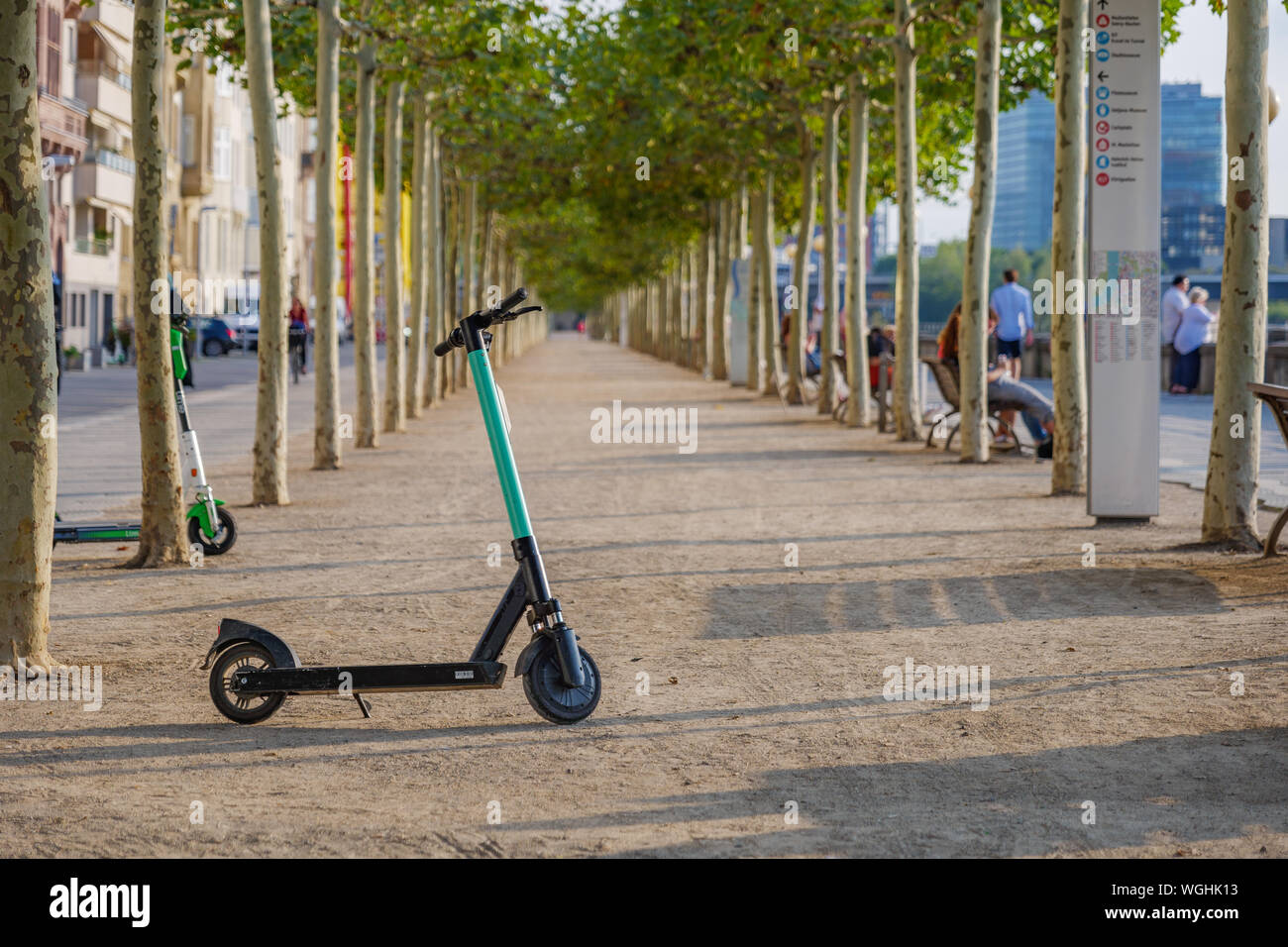 Scooter elettrici park passeggiata sul lungofiume del Reno a Düsseldorf, Germania con sottofondo di diminuire la linea in prospettiva degli alberi . Foto Stock