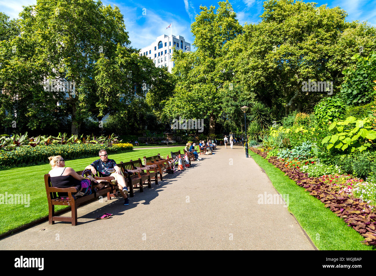 La gente seduta sulle panchine in estate a Victoria Embankment Gardens, London, Regno Unito Foto Stock