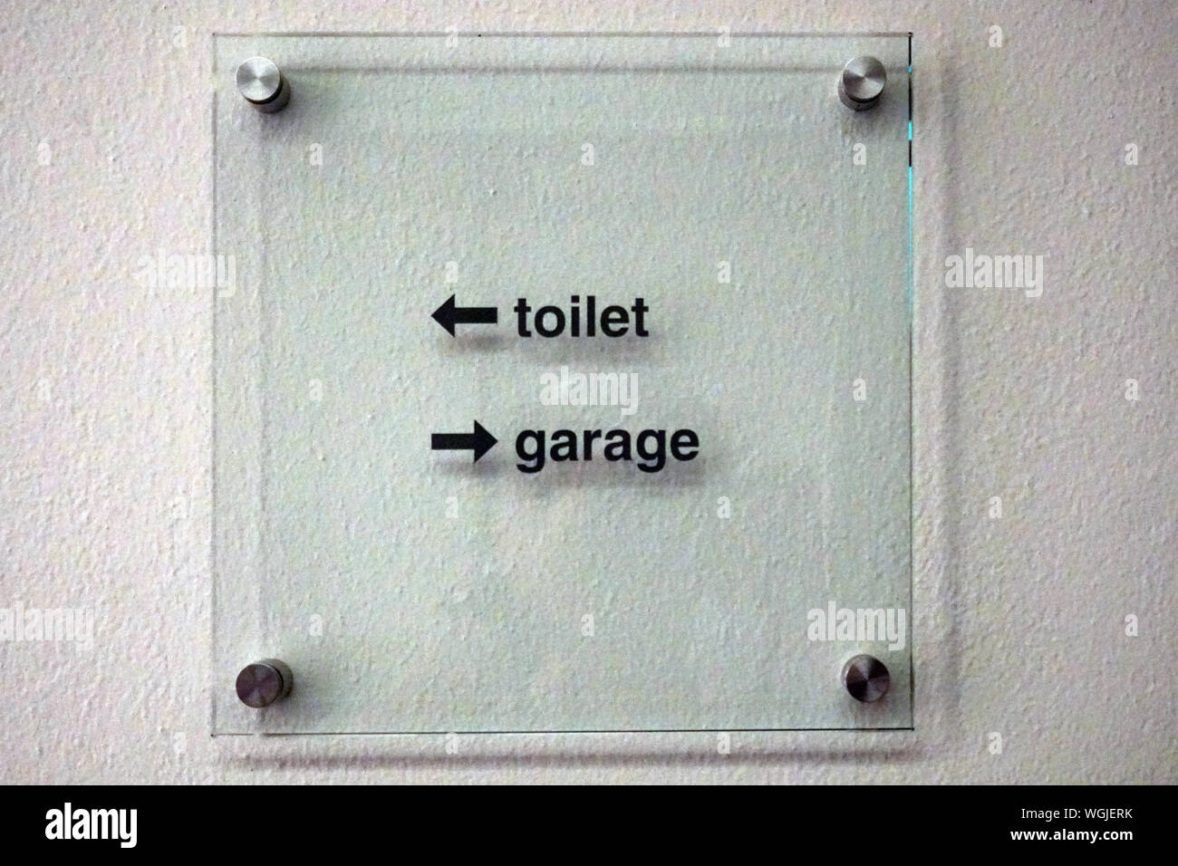 Il wc-garage segno con due frecce nella piazza di plexiglass appesi al muro bianco Foto Stock